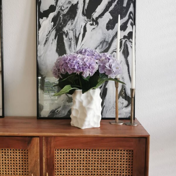 White 3D-printed sculptural vase with purple hydrangeas, placed next to brass candleholders and abstract painting