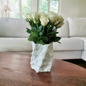 White 3D-printed sculptural vase with a dimpled surface, filled with a bouquet of white roses