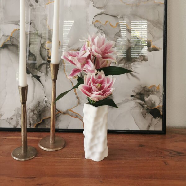 White 3D-printed sculptural vase with pink lilies placed on a wooden surface styled next to candlesticks