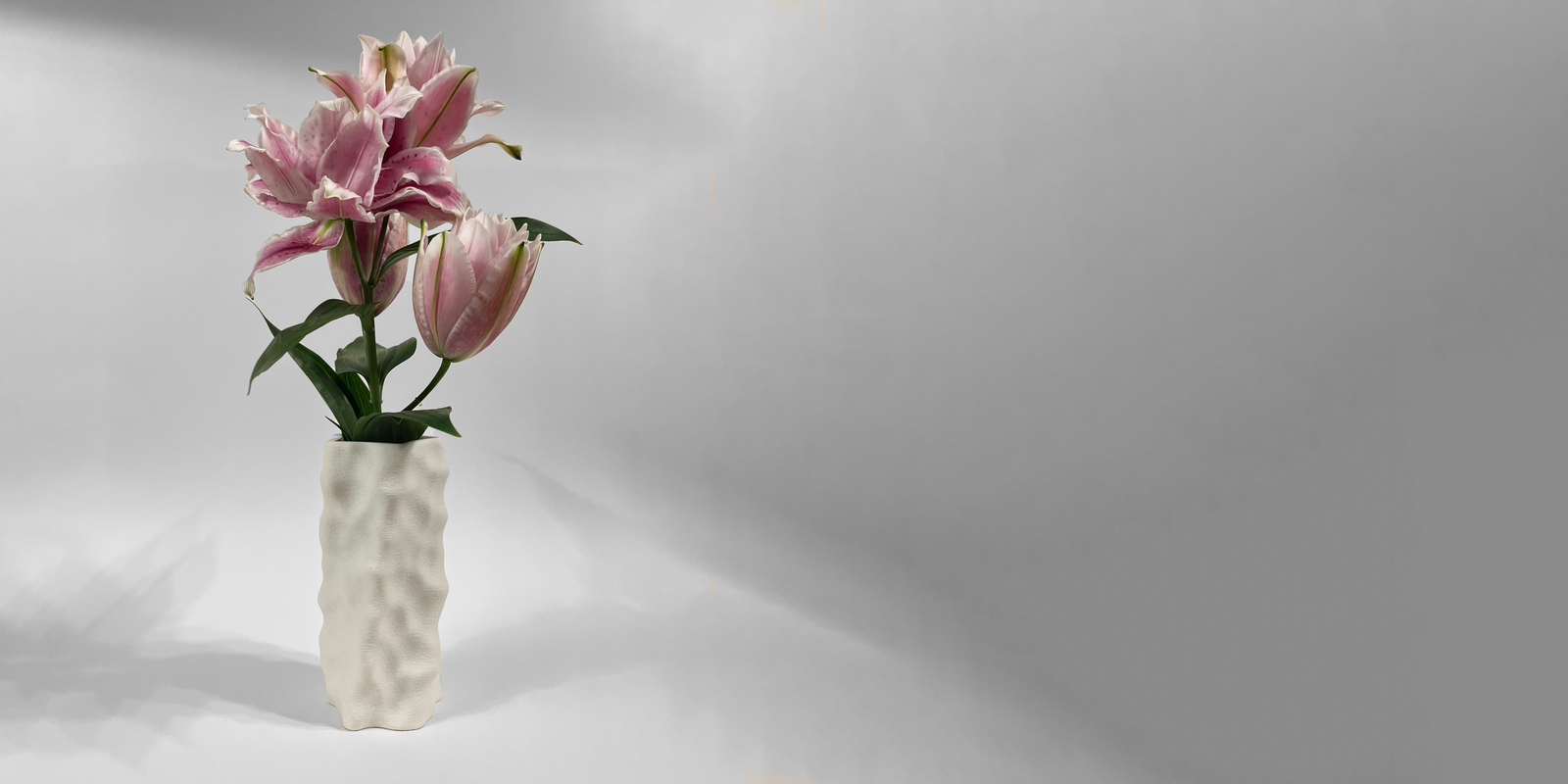 Tall white 3D-printed sculptural vase with a dimpled surface, holding pink lilies