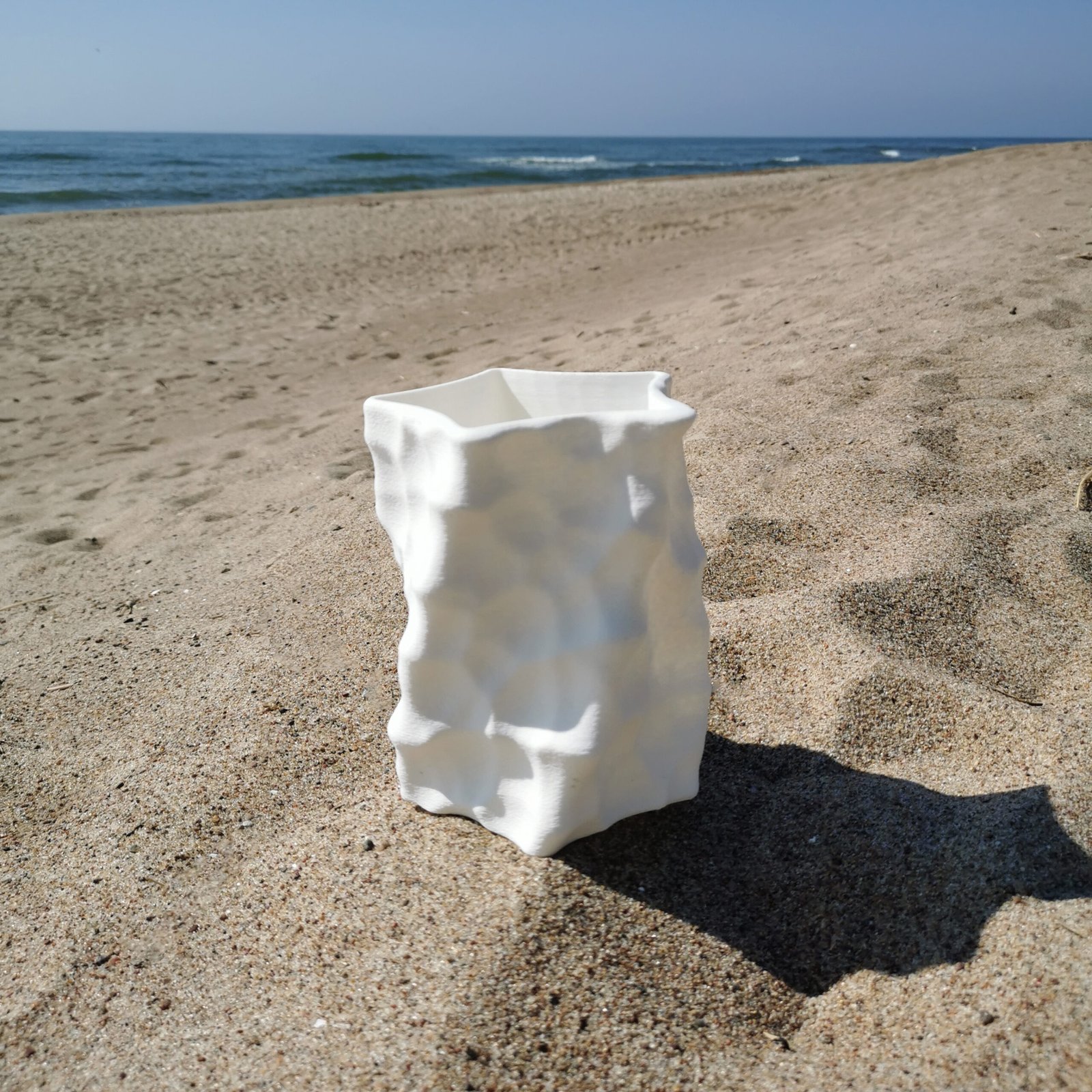 White 3D-printed sculptural vase with textured surface standing on a sandy beach